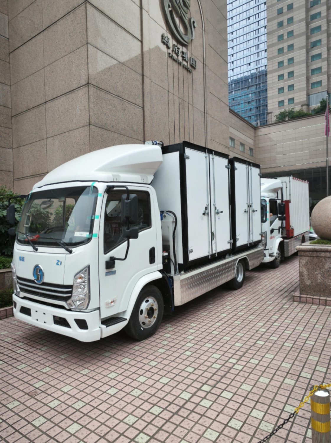 Two white Aeroswap S6 trucks parked outside an office tower